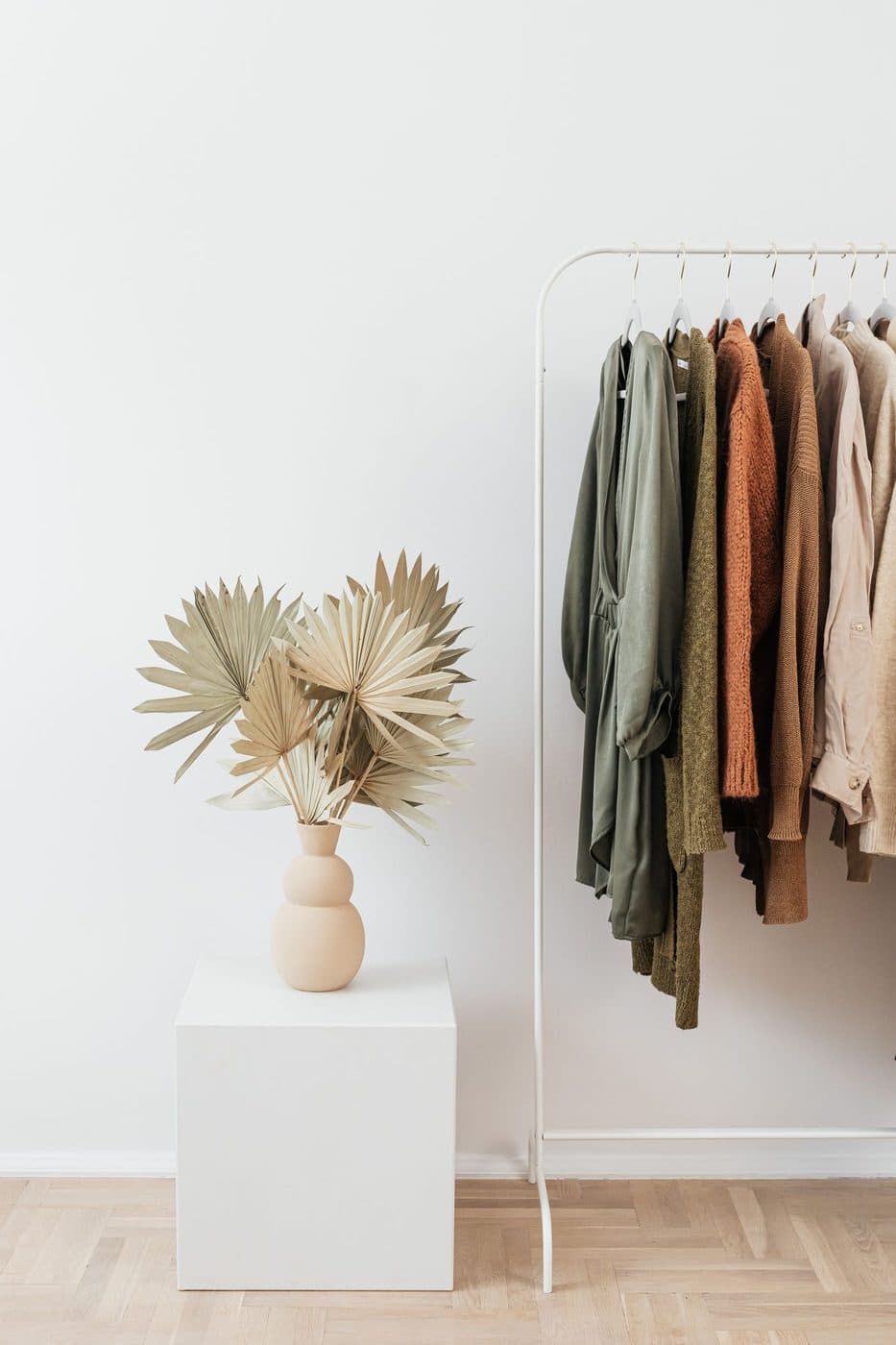 Knitted cardigans on a rail beside a vase of dried palm leaves