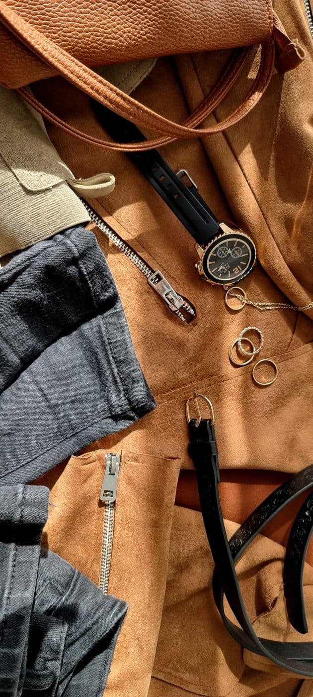 A suede jacket, leather belt and watch lying in sunlight