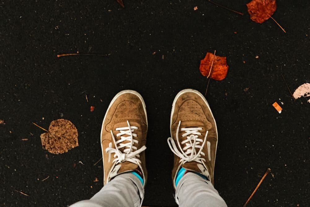 Suede sneakers on dark pavement scattered with autumn leaves