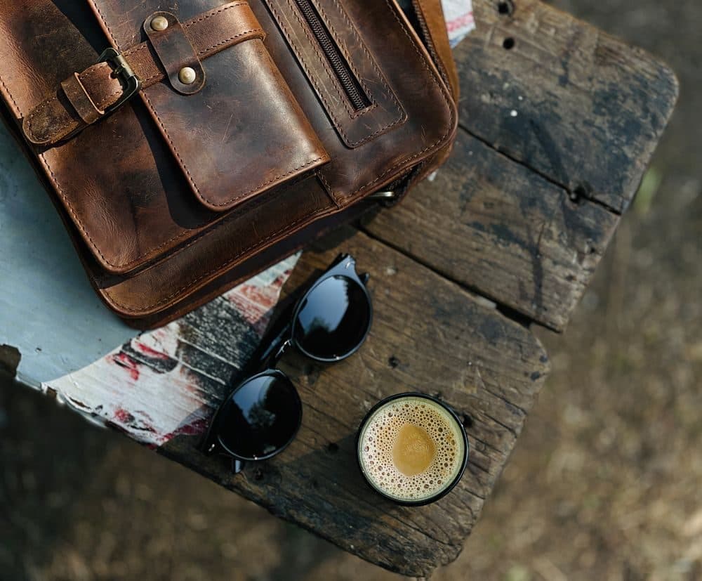 A leather satchel and sunglasses on a weathered wooden table